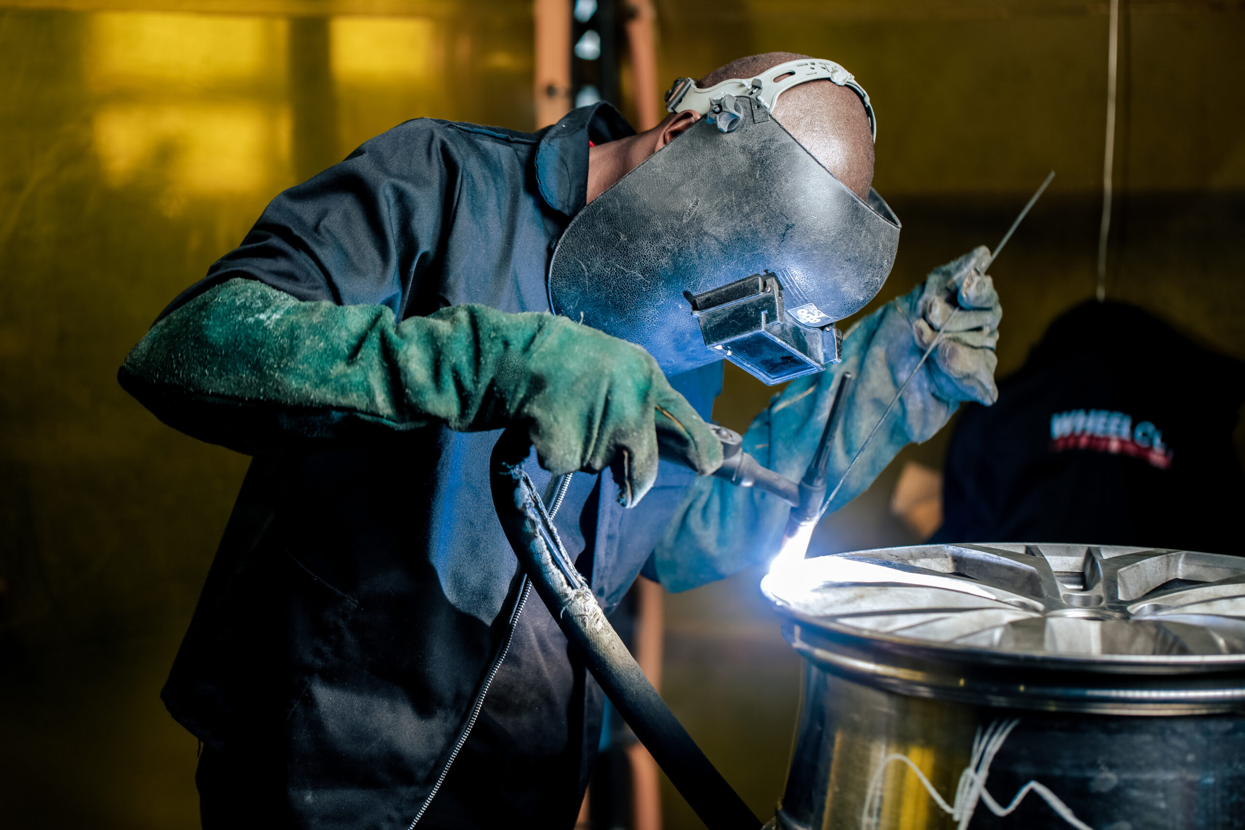 A wheel collision technician using a welding machine as part of the alloy wheel repair process