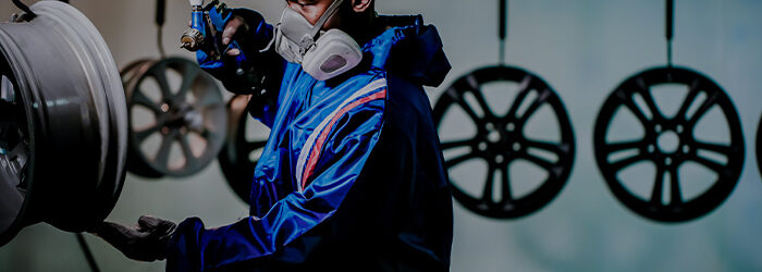 A wheel collision technician spraying paint on an alloy wheel